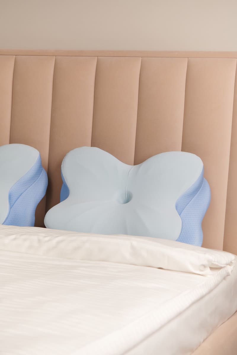 Contoured pillow seen head-on against an upholstered headboard, with the butterfly shape and centre well visible
